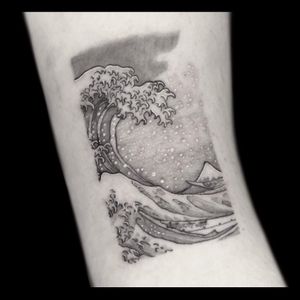 A stunning blackwork wave tattoo on the forearm, by the talented artist Drone. This illustrative piece captures the beauty and power of the ocean.