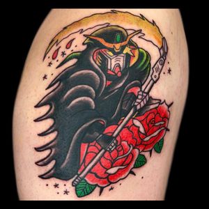 Illustrative traditional tattoo featuring a grim reaper with a scythe surrounded by flowers on the upper arm. By Drone.