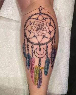 Adorn your lower leg with this stunning illustrative tattoo featuring a dreamcatcher, moon, and feather by Michaelle Fiore.