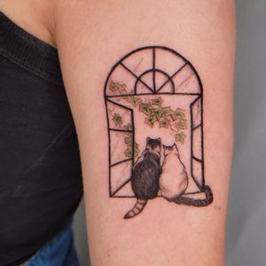 Get a unique blackwork tattoo by Erin featuring a cat, flower, and window, beautifully designed for your upper arm.