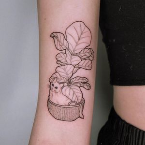Express your love for felines with this charming blackwork tattoo by Erin, featuring a playful cat, leaf, and basket design on your upper arm.