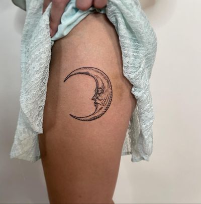 Elegant fine line moon tattoo on upper leg by artist Ermis Atzemoglou. Symbolizes cycles and transformation.