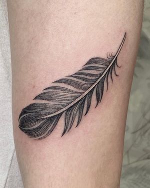 Elegant black and gray fine line feather tattoo on the upper leg, created by tattoo artist Sophie Rose Hunter.