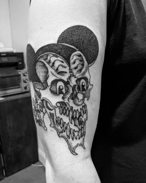Unique blackwork and illustrative tattoo by Shane featuring a skull and Mickey Mouse motif on the upper arm.