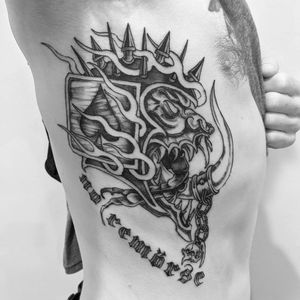 Unique blackwork ribs tattoo featuring a skull, quote, card, and chain design, executed with detailed illustrative lettering by talented artist Shane.