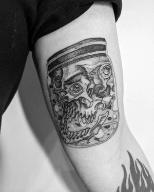 Unique illustrative tattoo featuring a skull, bottle, and jar on the upper arm. Done by the talented artist Shane.