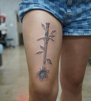 Experience a striking blend of blackwork and illustrative styles with a beautiful flower and sword motif, expertly done by Lawrence.