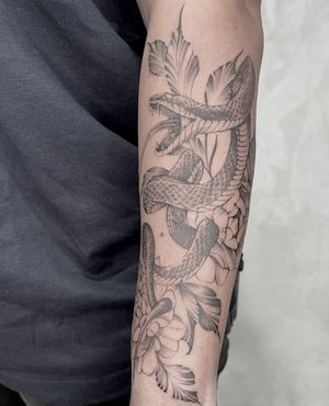 Get a stunning blackwork snake and flower forearm tattoo by Lawrence. A beautiful and intricate illustrative design.