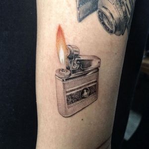 Get a stunning illustrative tattoo of a lighter by Lim on your upper arm. Perfect for those who appreciate realism in their ink.