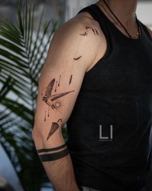 This upper arm tattoo by Ali Aman features a striking blend of geometric shapes, micro-realism, and intricate patterns, with a stunning sun, bird, and umbrella motif.