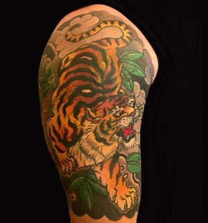 Exquisite illustrative upper arm tattoo featuring a fierce tiger and delicate leaf motifs, by the talented artist Kiko Lopes.