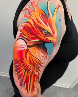 Embrace the mythical phoenix with a vibrant watercolor design by Cloto.tattoos on your upper arm. Stand out with this illustrative masterpiece.