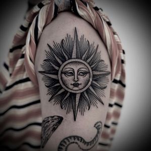 Intricate black and gray dotwork design featuring a sun and moon in a circular motif by Lamat. Ideal for upper arm placement.