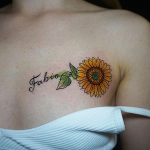 Intricate small lettering combined with vibrant watercolor elements create a stunning floral design on the chest, expertly crafted by Aygul.