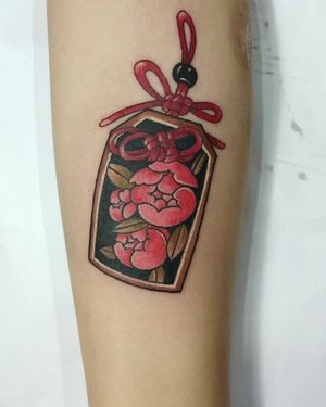 A stunning neo-traditional forearm tattoo by Avi featuring a beautiful flower, charm, and omamori designs in an illustrative style.