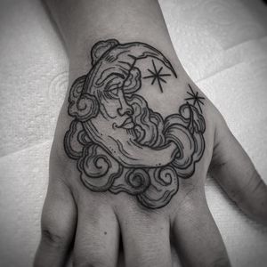 Elegant black and gray fine line tattoo featuring a moon and star motif, beautifully crafted by artist Lamat on the hand.