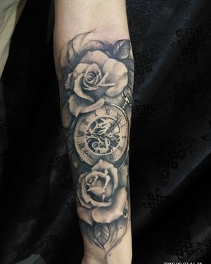 Experience the beauty of a black and gray illustrative tattoo featuring elegant flowers and a detailed clock by the talented artist Avi.