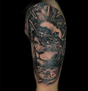 Impressive black and gray piece with realistic lion, watch, and intricate lettering by Avi. Adorn your upper arm with this unique masterpiece.