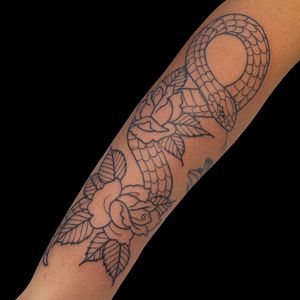 Elegant forearm tattoo by Letitia Mortimer featuring a intricate snake, delicate flower, and leaf design.