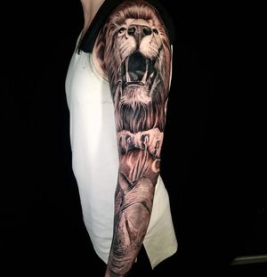 Get an impressive black and gray sleeve tattoo featuring a detailed lion and rhino design by Mauro Imperatori.