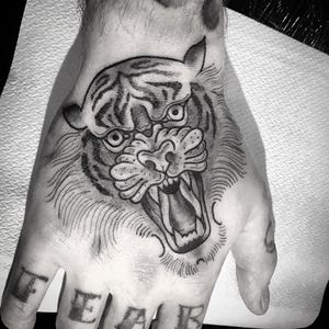 Capture the fierce beauty of a tiger with intricate fine line detailing in this hand tattoo by Matthew Ono. Black and gray stripes bring the design to life.