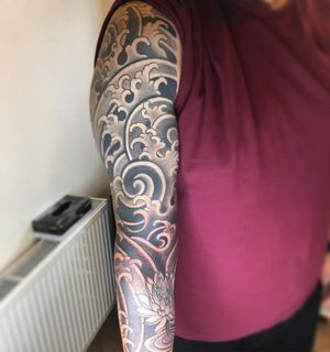 Experience the beauty of Japanese art with this black and gray illustrative sleeve tattoo by Kiko Lopes, featuring delicate flowers and rolling waves.