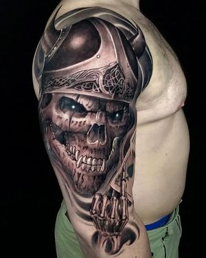 This upper arm tattoo by Mauro Imperatori features a detailed black and gray skull inspired by Viking mythology.