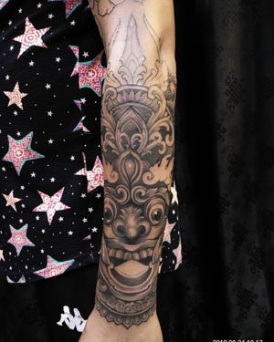 Experience the beauty of Japanese art with this stunning forearm tattoo featuring intricate patterns, a mysterious mask, and piercing eyes by Avi.