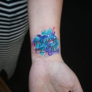 Unique small lettering tattoo featuring galaxy motif on forearm by Aygul. Colorful and dreamy design.