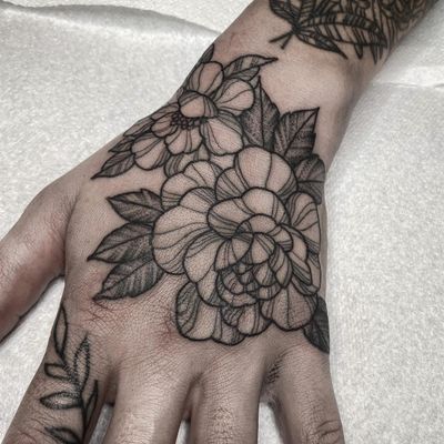 Elegant black and gray tattoo of a delicate flower and leaf design on the hand by artist Lamat.