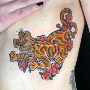 Experience the fierce grace of a tiger intertwined with delicate flowers on your ribcage. By artist Matthew Ono.