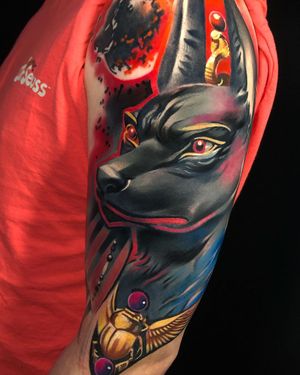 A stunning illustrative tattoo featuring a dog, snake, Anubis, and beetle on the upper arm, by Cloto.tattoos.