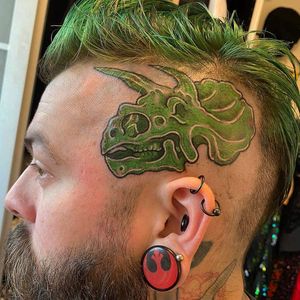 Get inked by Matthew Ono with a vibrant new school dino design on your side face. Stand out and make a statement with this bold tattoo!