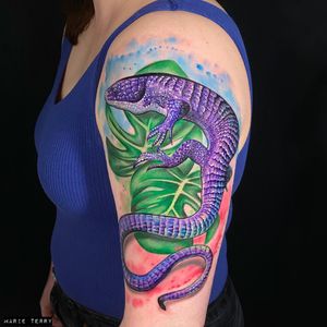 Get a stunning new school tattoo of a lifelike lizard and intricate leaf design by the talented artist Marie Terry.