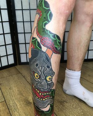 A stunning illustrative tattoo on the lower leg featuring a fierce snake and a haunting Hannya mask, by artist Kiko Lopes.