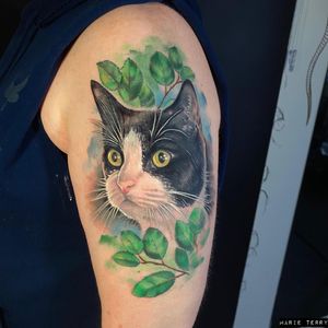 Get a stunning piece by Marie Terry featuring a lifelike cat and delicate leaf design on your upper arm.
