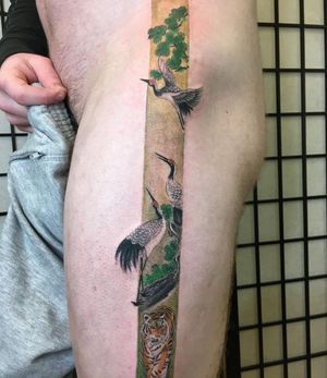 A stunning illustrative tattoo by Kiko Lopes featuring a powerful tiger, graceful heron, majestic tree, and intricate frame on the upper leg.