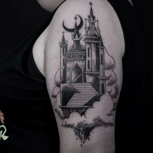 Experience the magic of a black and gray castle tattoo by Luca Salzano on your upper arm. Add a touch of fantasy to your style.