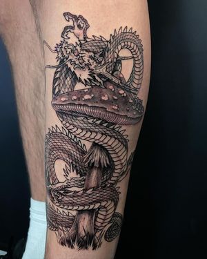 Intricate black and gray design by Fernando Joergensen, blending a fierce dragon with a whimsical mushroom motif on the lower leg.