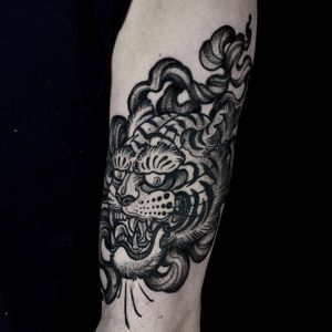 Get a fierce and elegant black and gray Japanese tiger tattoo with bold stripes on your forearm by the talented artist Lamat.