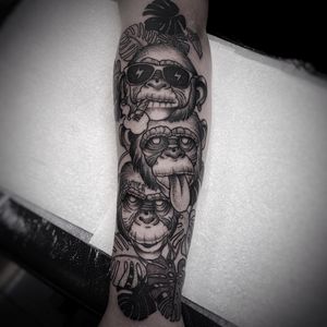 Unique black and gray dotwork tattoo on forearm featuring a stylish monkey wearing glasses and holding a leaf, by artist Lamat.