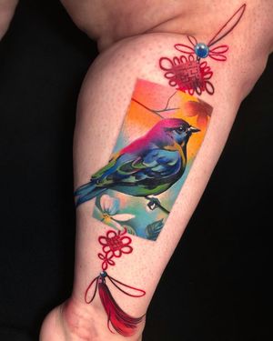 Beautiful lower leg tattoo featuring a realistic bird and flower design, inspired by omamori charms. By Cloto.tattoos.
