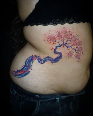 Vibrant watercolor tree and flower tattoo on ribs by Aygul, blending nature and art beautifully.