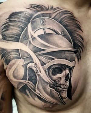 A striking black and gray illustrative tattoo of a skull wearing a helmet, created by talented artist Avi.