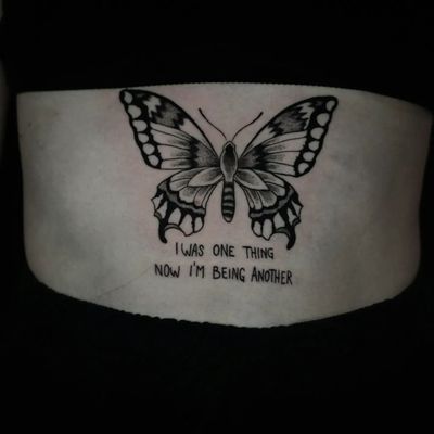 Delicate black and gray butterfly tattoo with small lettering quote on the back by Luca Salzano.