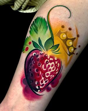 Illustrative upper arm tattoo of a vibrant watercolor strawberry topped with a delicate crown by Cloto.tattoos.