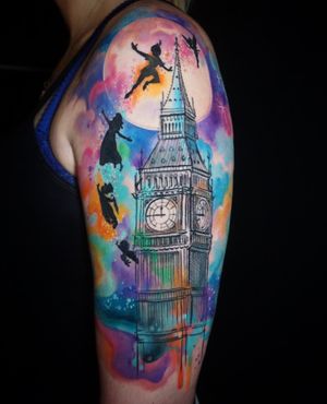 Capture the magic of Neverland with this stunning watercolor tattoo featuring Peter Pan and sketchwork of Big Ben by Aygul.