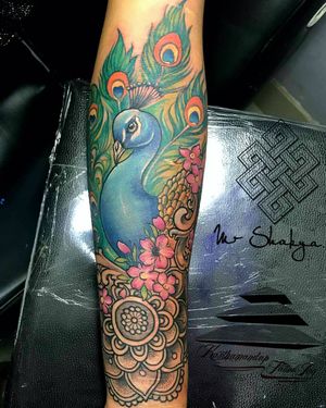 Avi's neo-traditional forearm tattoo features a stunning peacock surrounded by delicate sakura flowers, feathers, and intricate patterns.