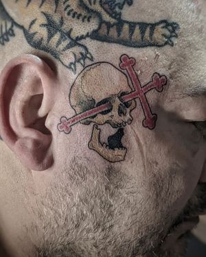 Illustrative tattoo by Luca Salzano featuring a bold skull and cross design on the side of the face.