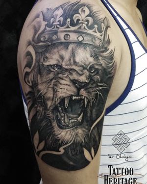 Intricately detailed black and gray lion with a majestic crown, beautifully rendered on the upper arm by artist Avi.